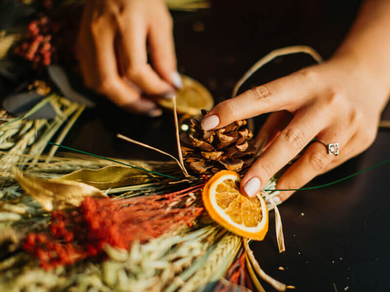 Pine cone, dried orange and dried florals being made into a wreath.